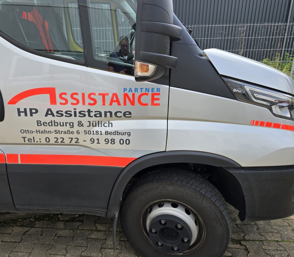 Ein weißer Lastwagen mit orangefarbener Beschriftung steht auf einem Parkplatz.