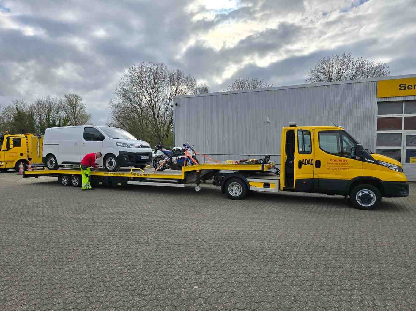 Gelber Lastwagen mit einem Auto auf der Ladefläche.