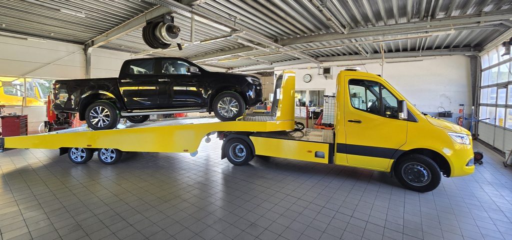 Ein gelber Lastwagen wird auf einen Flachbett-Lkw geladen.