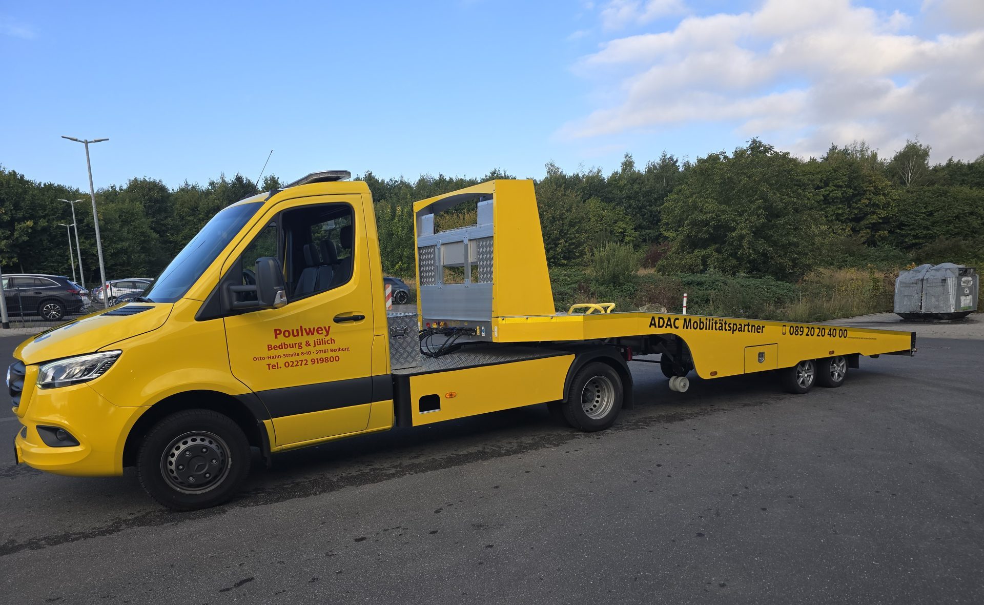 Gelber Lastwagen mit einem flachen Anhänger auf einer Straße.