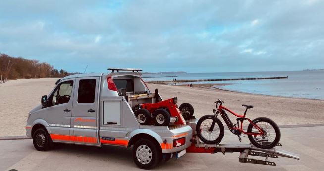 Ein Van mit einem Fahrrad auf der Rückseite parkt am Strand.